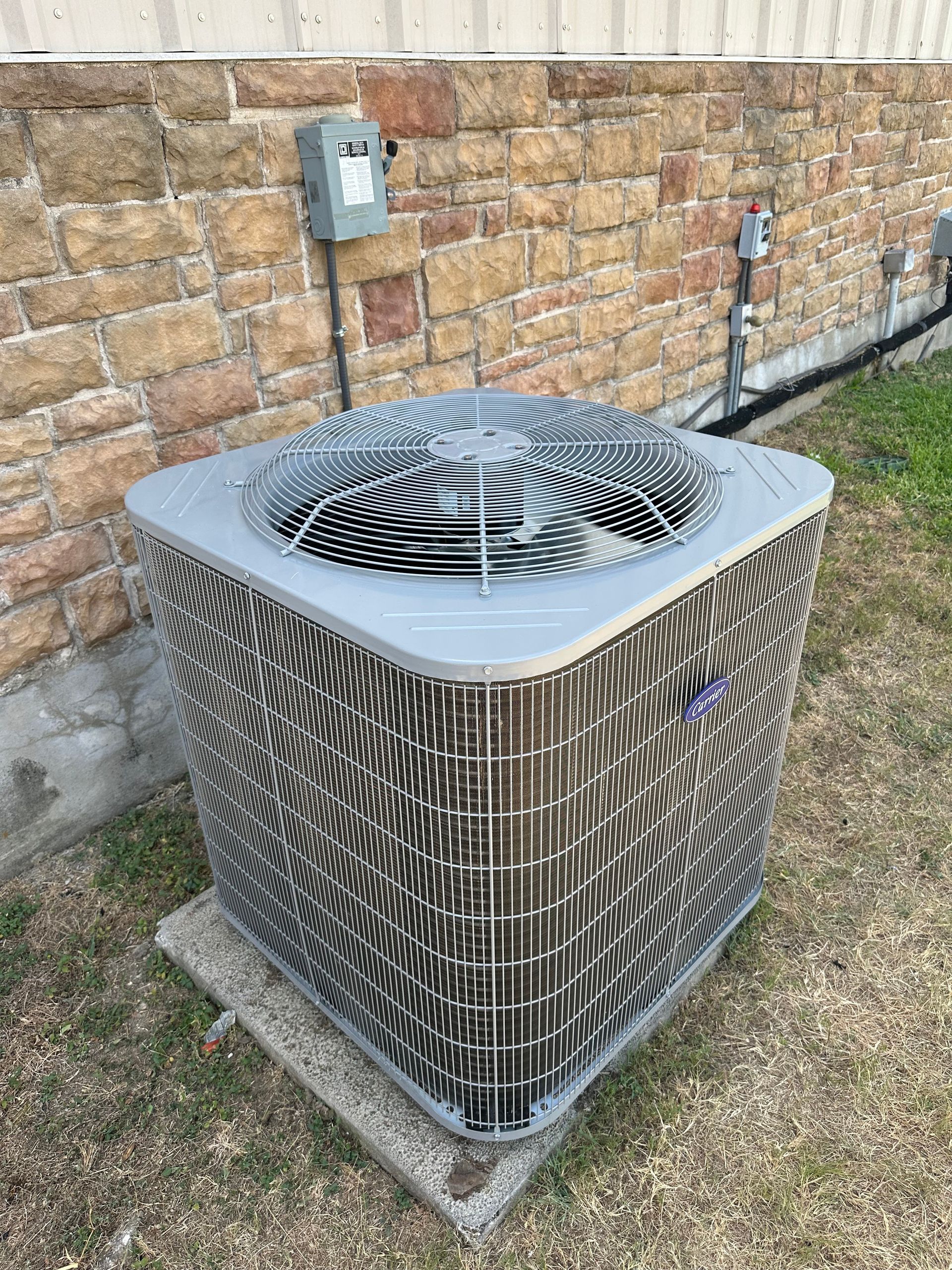 A large air conditioner is sitting in front of a brick wall.