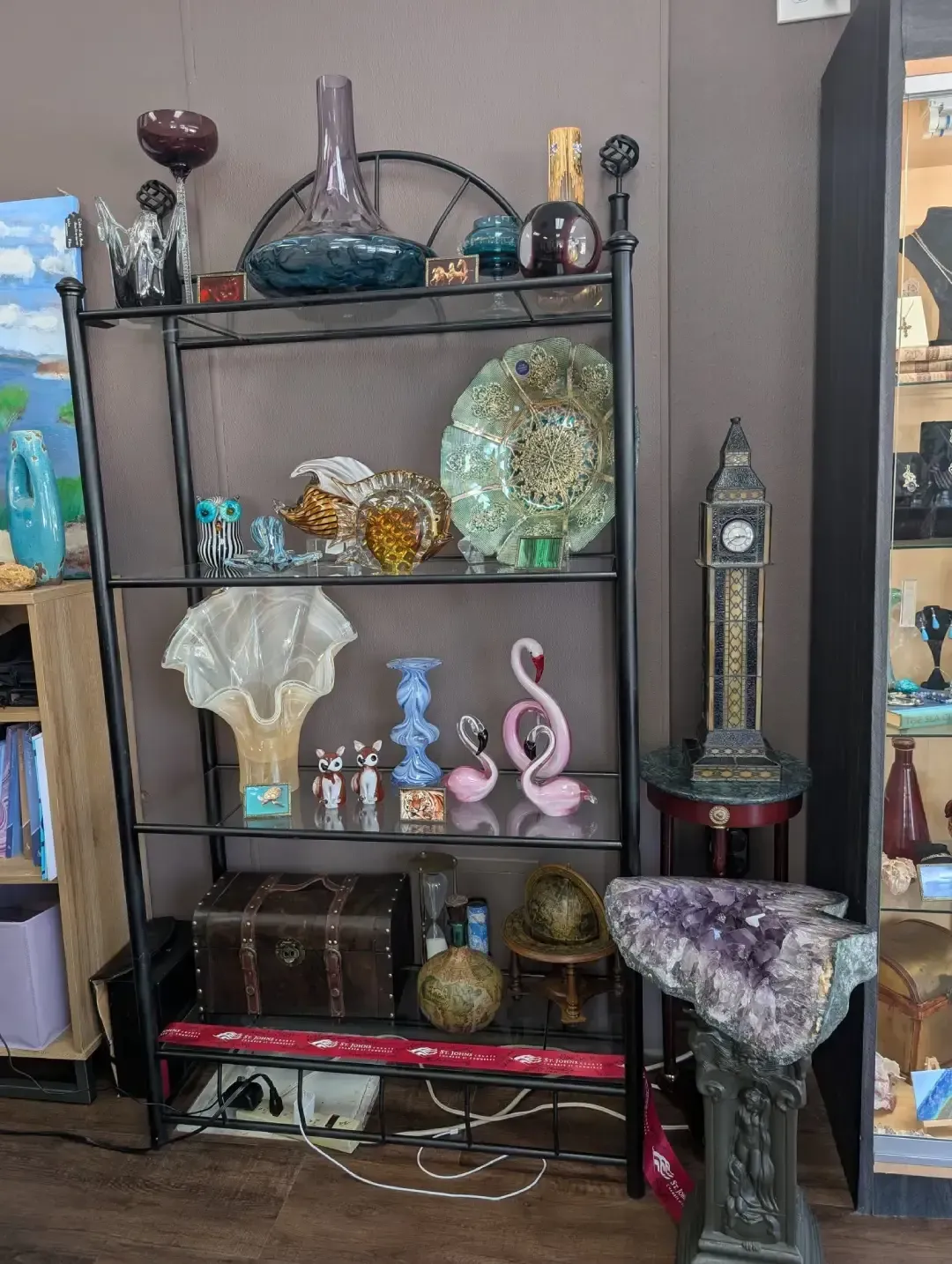A black metal display shelf holds various decorative items, including vases, figurines, and a chest, next to a clock stand.