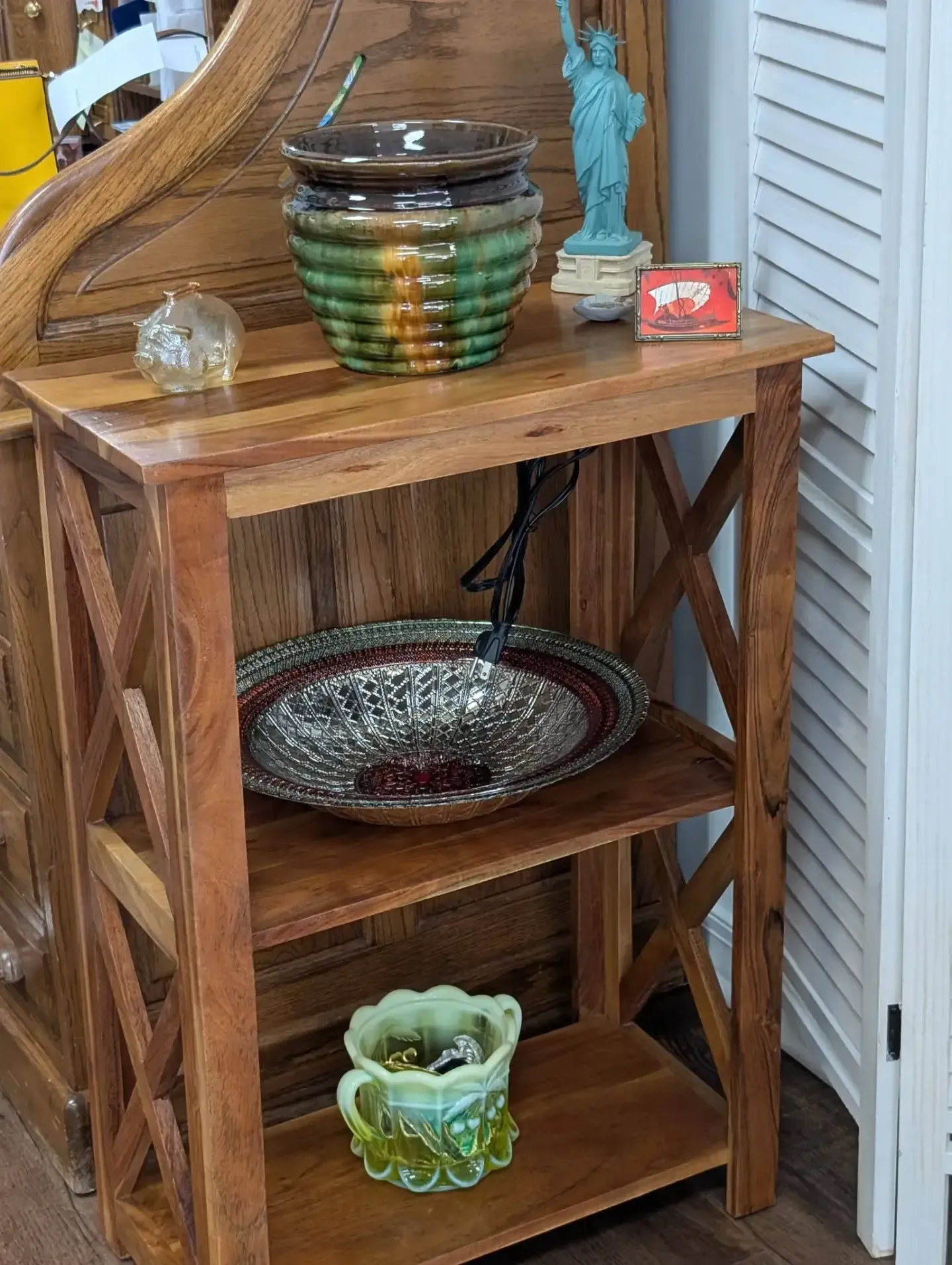 A three-tiered wooden shelf holding decorative bowls, a small Statue of Liberty replica, and miscellaneous trinkets.