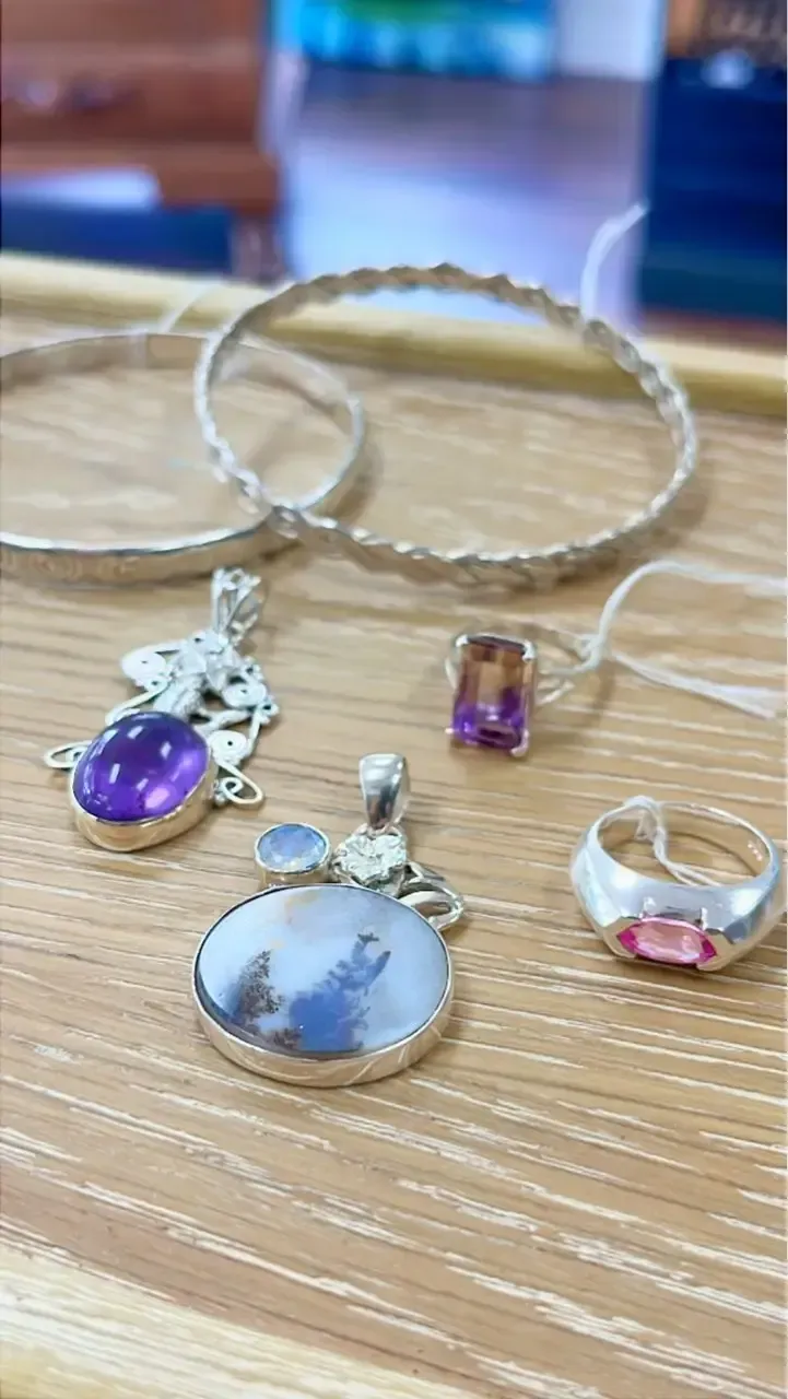 A collection of silver jewelry, including two bracelets, two gemstone pendants, and two rings on a wooden surface.