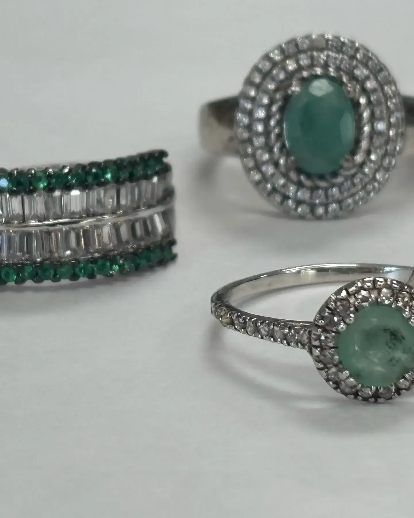 Three silver rings with green gemstones and small clear stones displayed on a plain white surface.