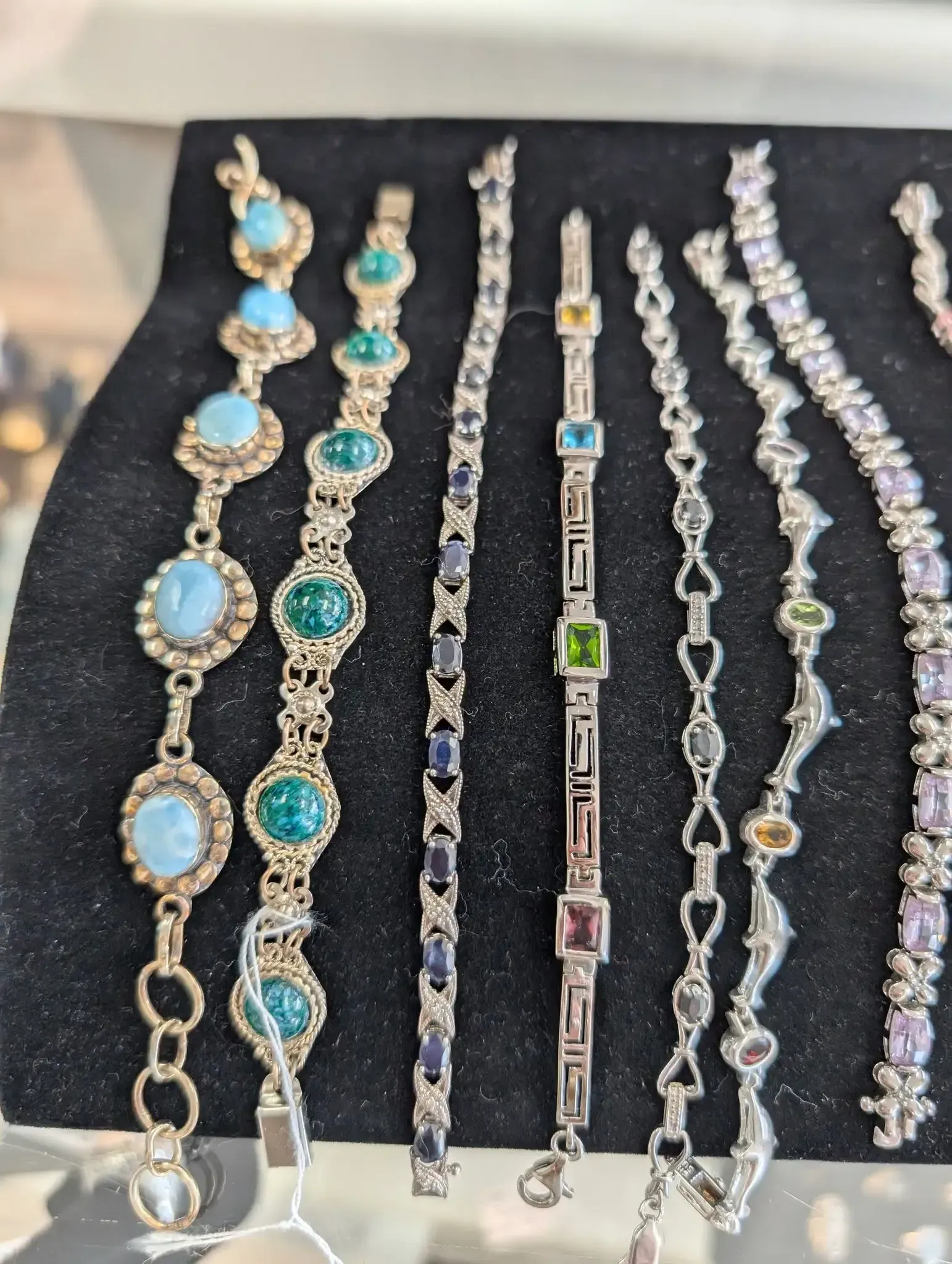 A selection of eight assorted gemstone and metal bracelets arranged side-by-side on a black display stand.