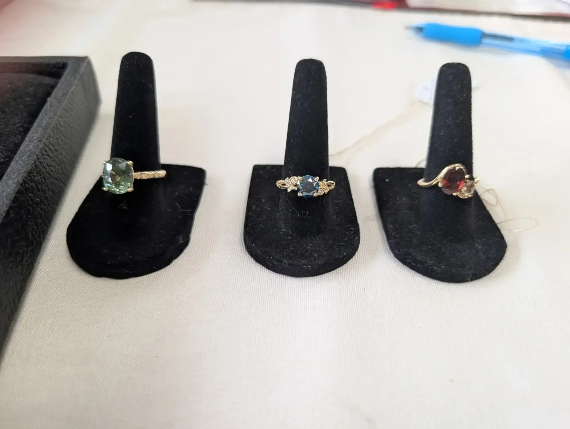 Three gold rings with green, blue, and red gemstones on black stands