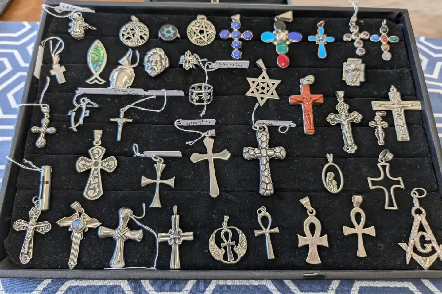 A collection of various metal cross and religious symbol pendants arranged in a velvet-lined display case.