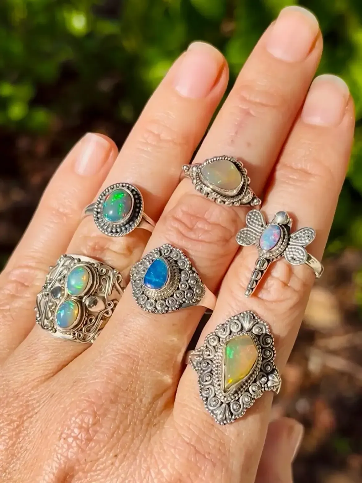 Hand wearing multiple silver rings with opal gemstones