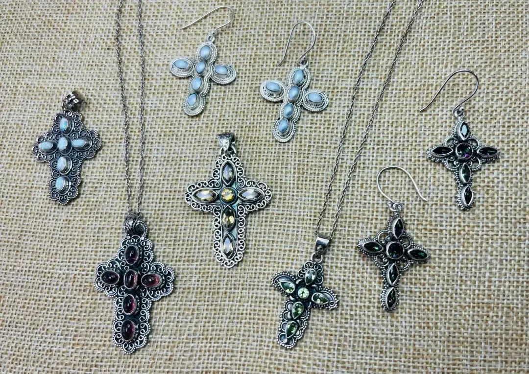 A collection of silver cross jewelry, including three necklaces, two pairs of earrings, and one loose pendant on burlap.