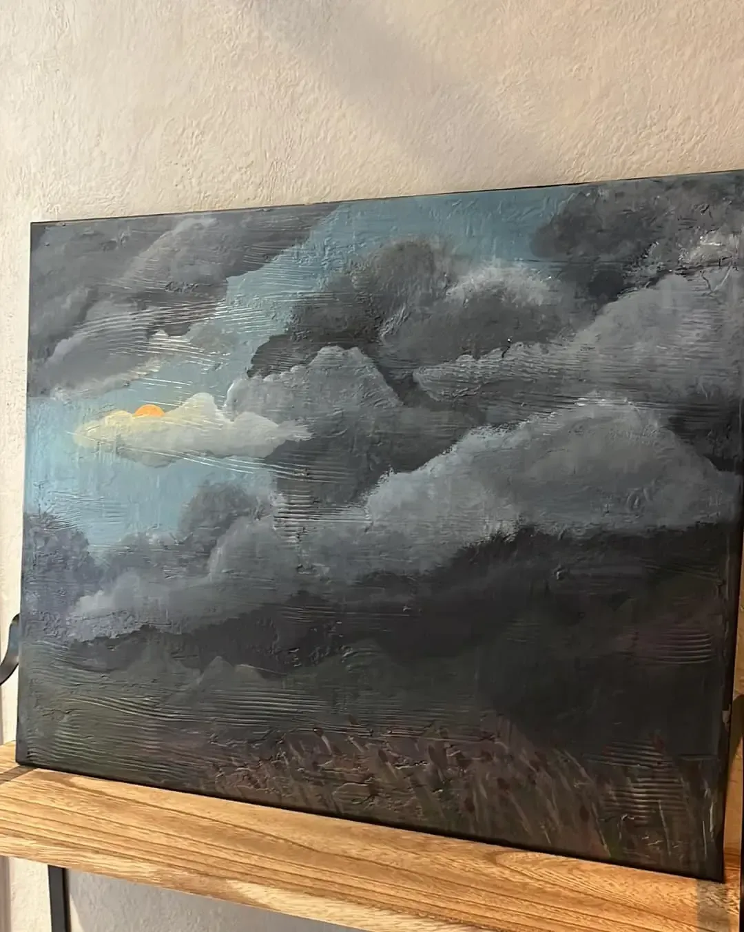 An oil painting depicts dark, textured storm clouds hanging low over a landscape with a small patch of golden light.