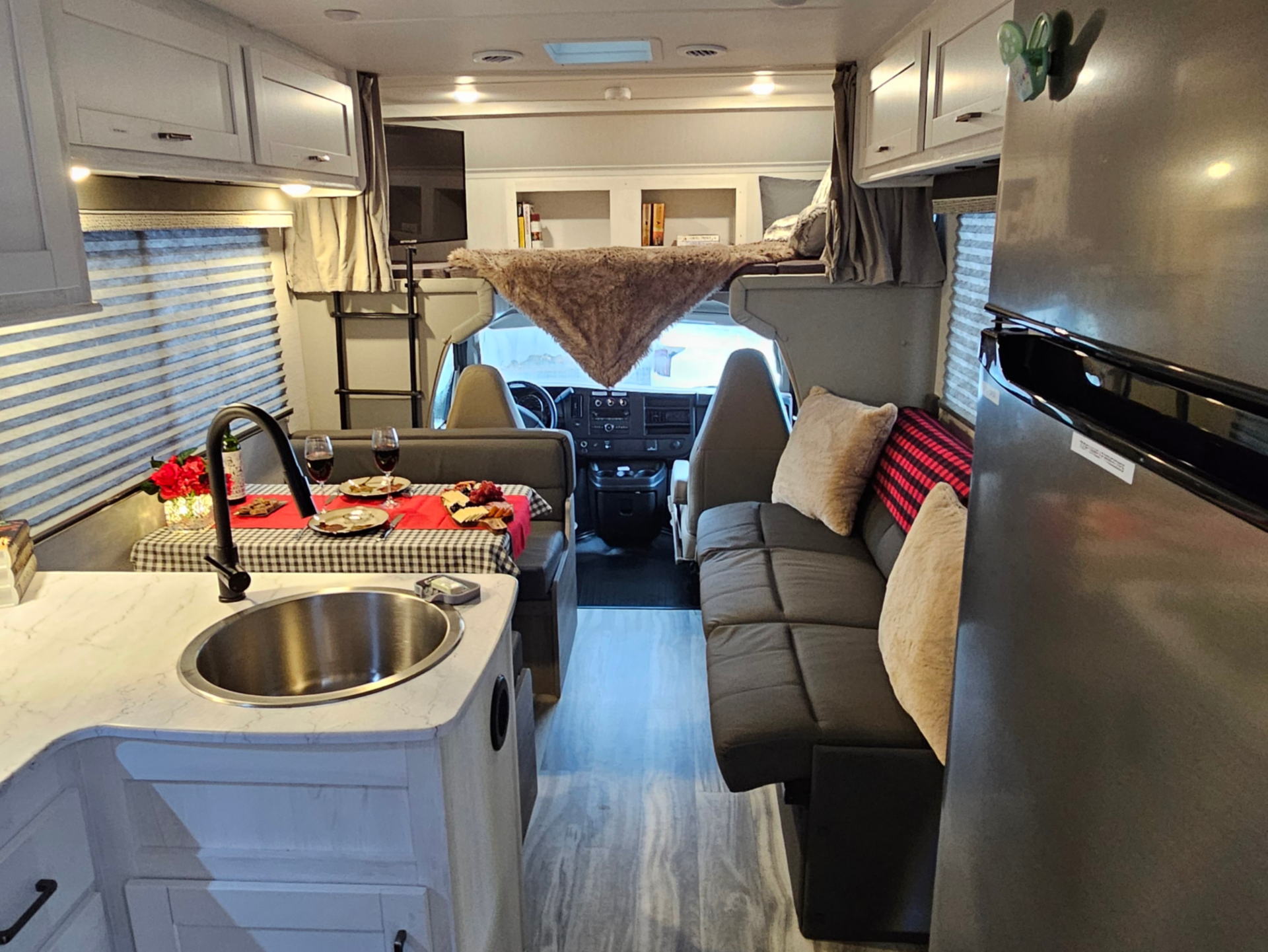 A kitchen in a rv with a sink , refrigerator , and couch.