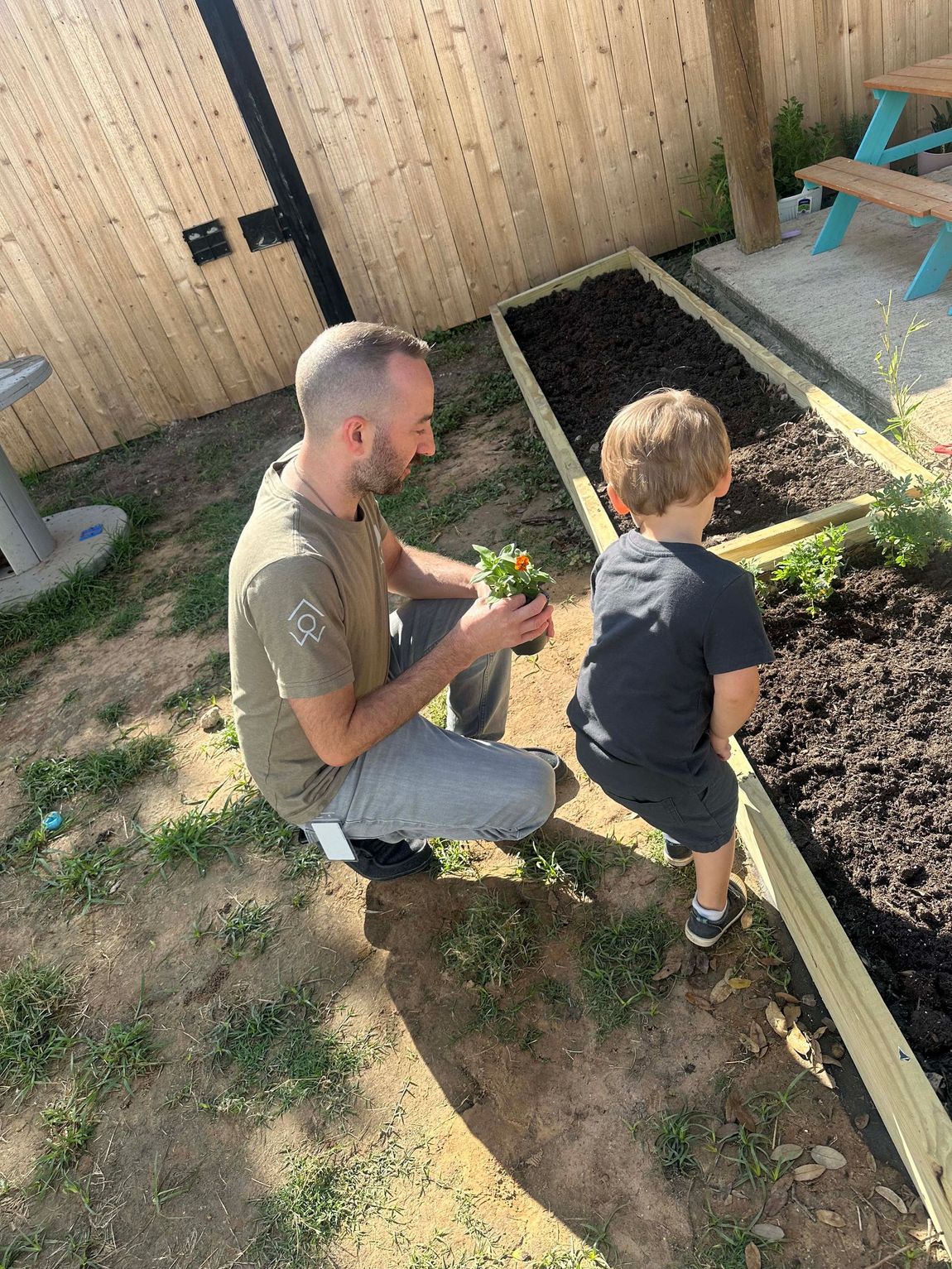 A man and a boy are kneeling in a garden.