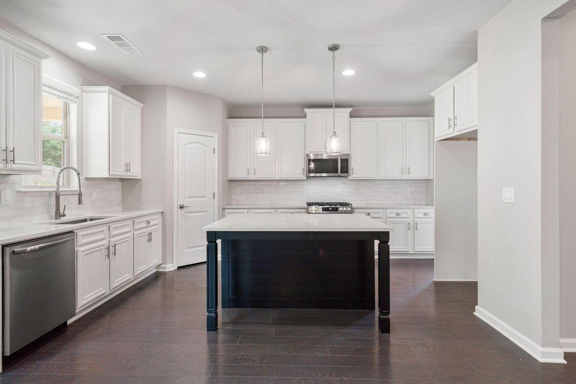 Modern kitchen with white cabinets, dark island, stainless steel appliances, and dark wood floors.