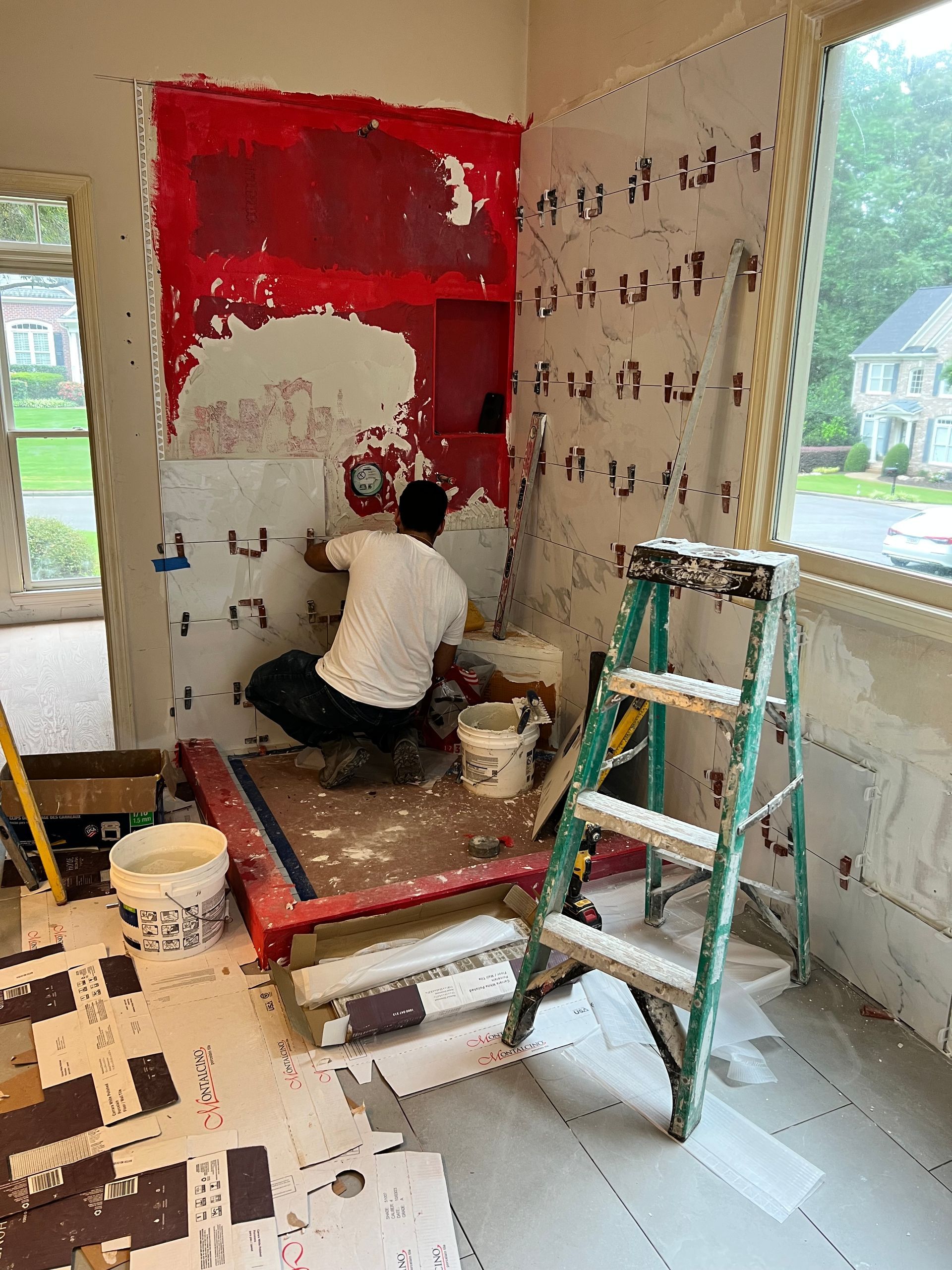 Person tiling a bathroom wall with red waterproofing. Construction site.