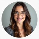 Woman with glasses smiles warmly, brown hair, grey patterned top.