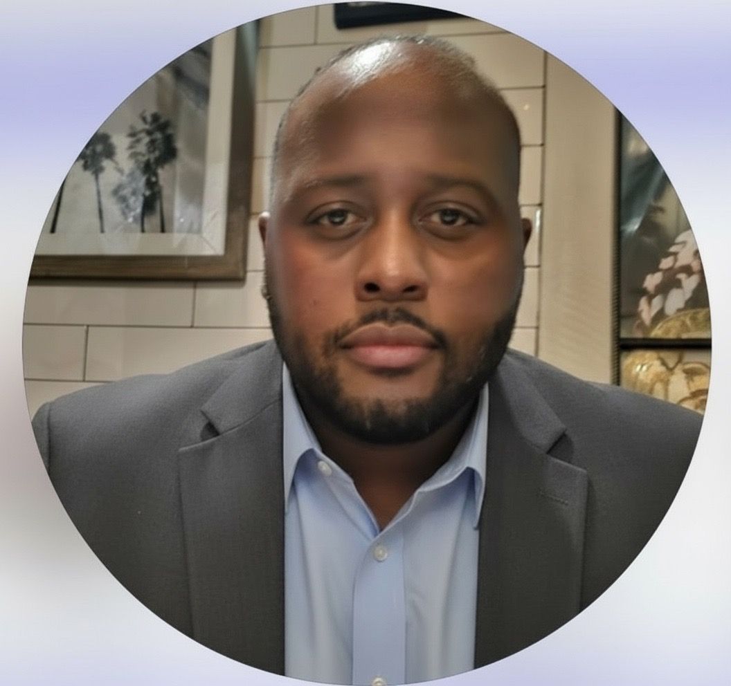 A Black man in a suit and button-down shirt looks at the camera.