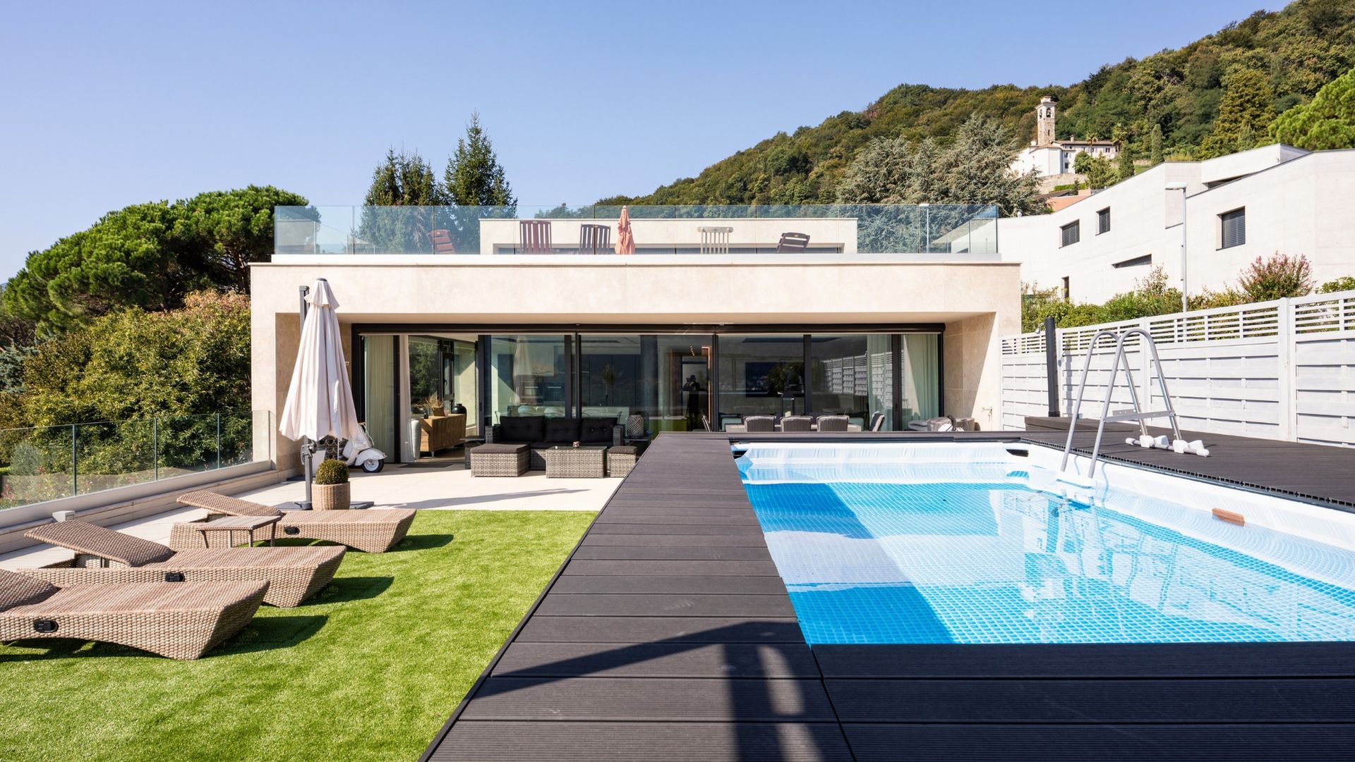 Modern home with pool and mountain view. Poolside deck with lounge chairs, green lawn, and blue sky.