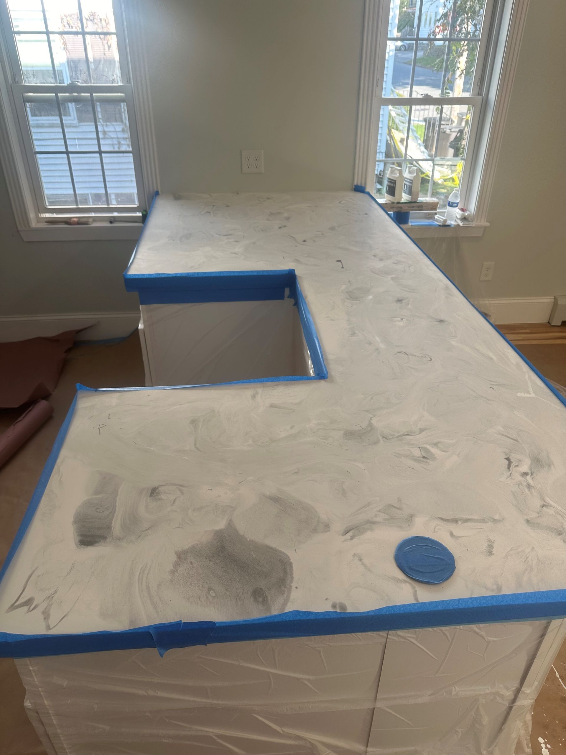 A kitchen counter is being painted in a room with a window.