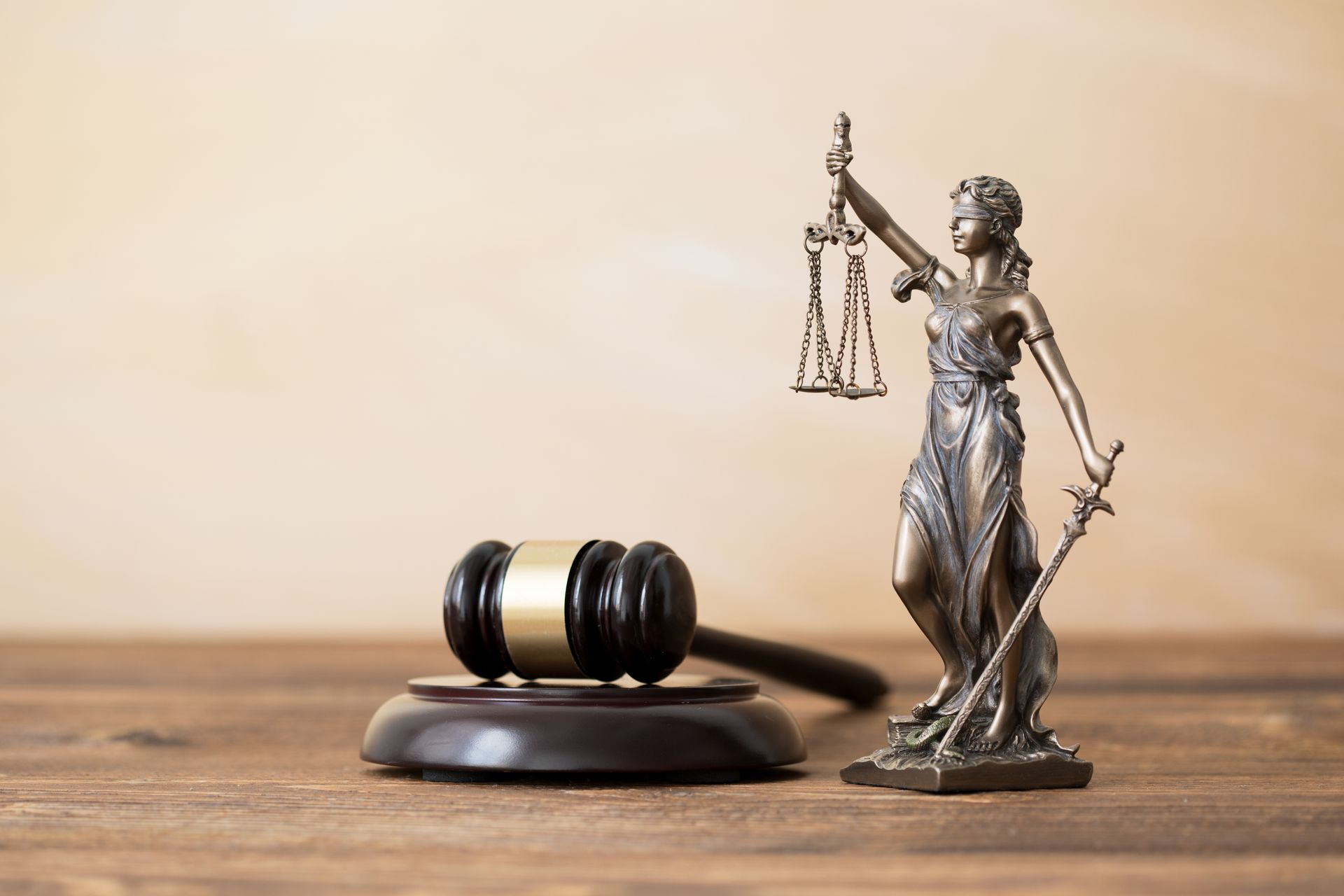 A bronze statue of Lady Justice holding scales stands beside a wooden gavel on a rustic wooden table.