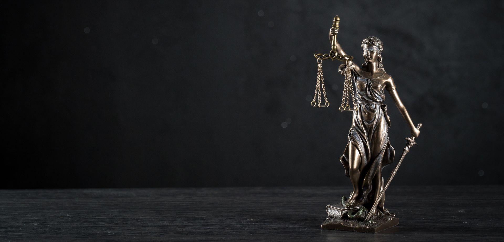 Bronze Lady Justice statue with scales and sword on dark background symbolizing law and fairness.