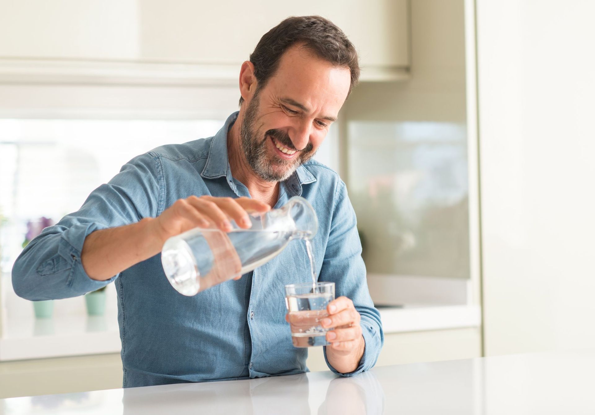 A man is pouring water from a pitcher into a glass.