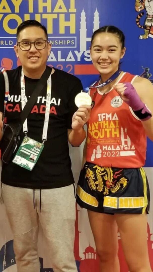 Man and smiling young woman in Muay Thai gear, holding medal, Malaysia 2022.