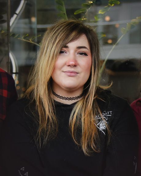 Woman with long blonde hair, wearing a black choker and sweatshirt, looking at the camera.