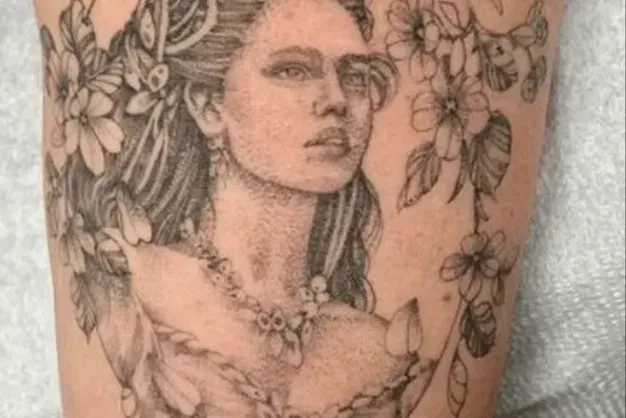 Black ink tattoo of a woman with flowers in her hair and around her.