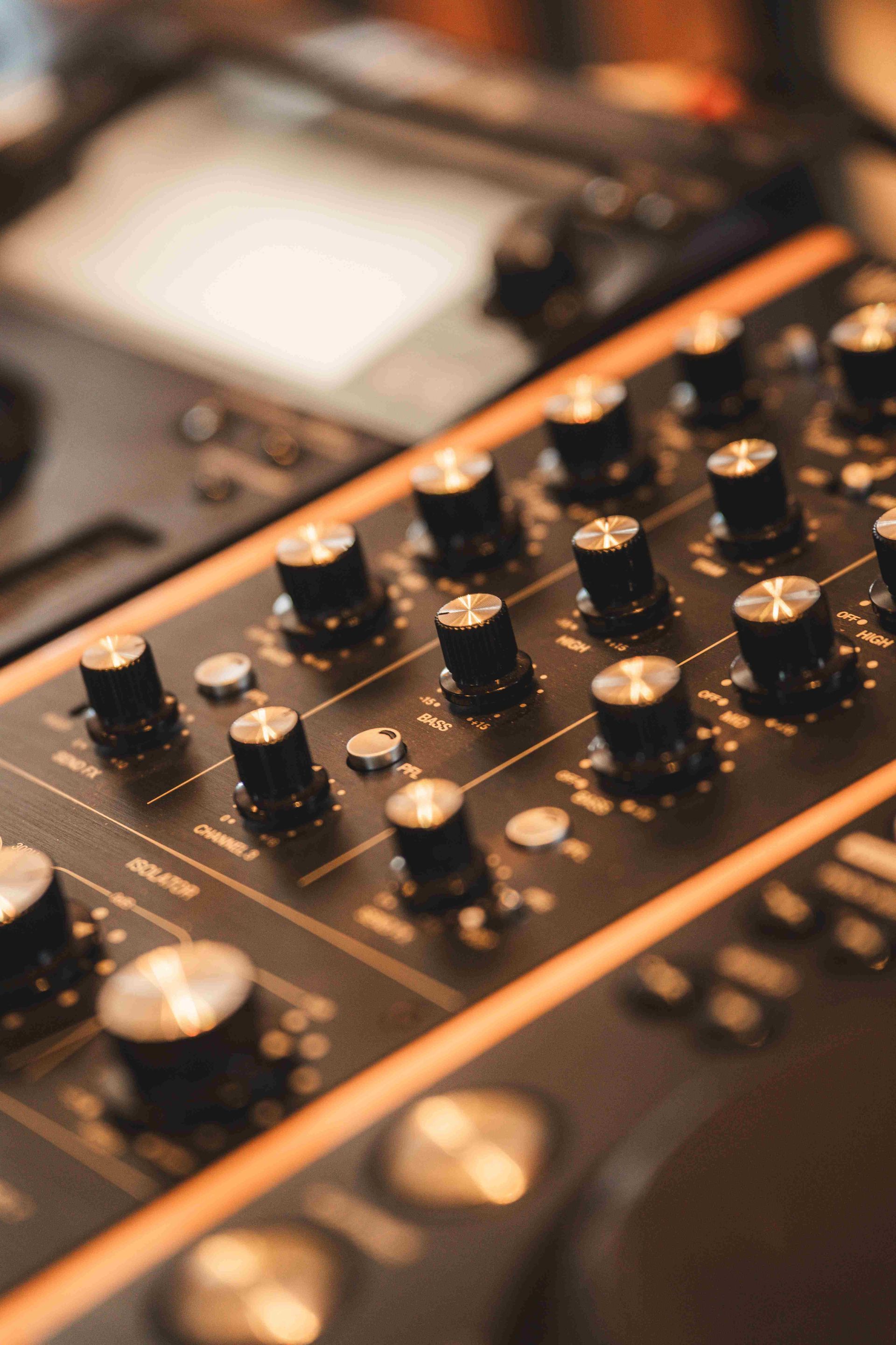 Uma visão aproximada e em ângulo de um console de mixagem de DJ preto com vários botões e controles, iluminado por luz quente.