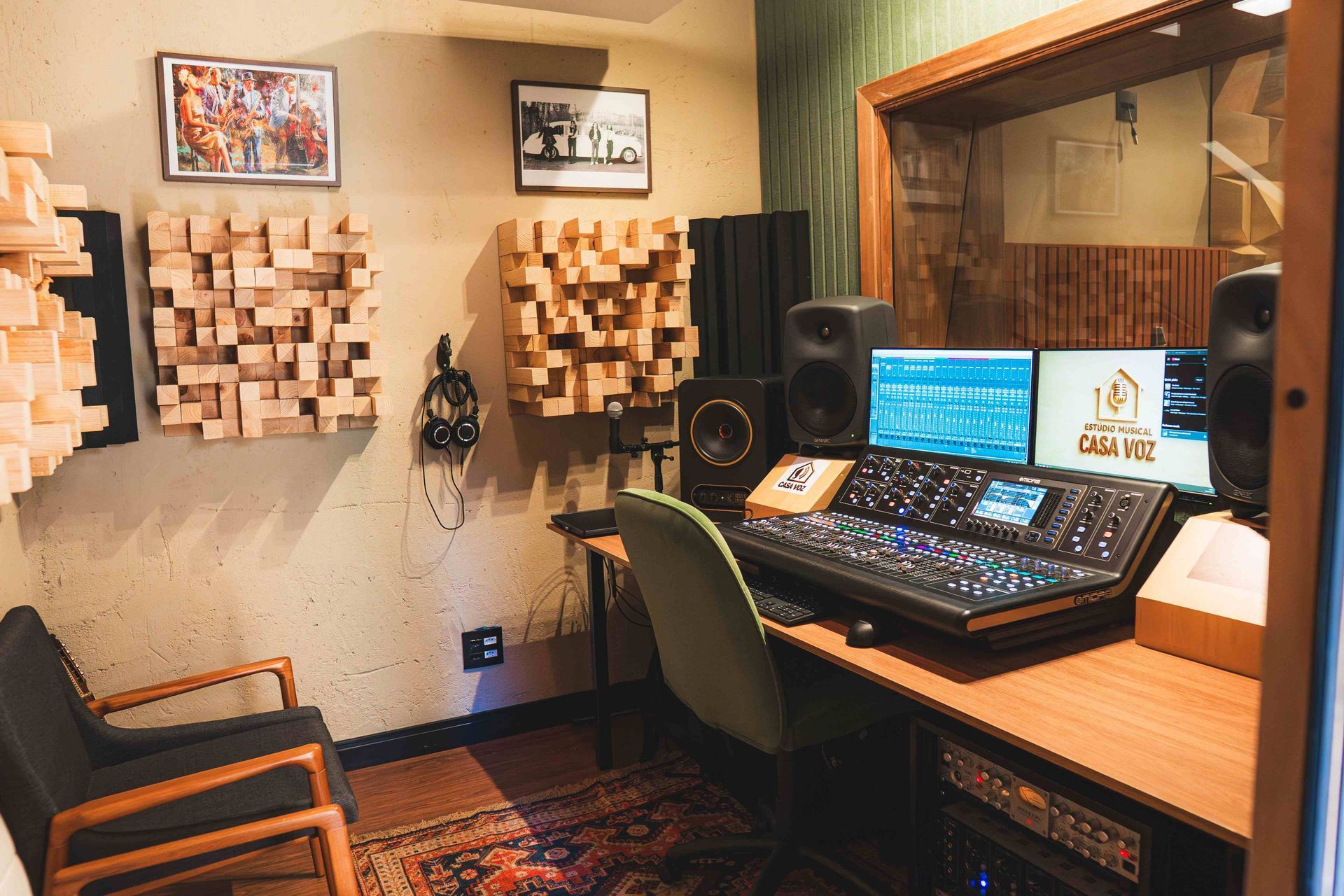 Um estúdio de gravação de som com mesa de mixagem, dois monitores, painéis acústicos de madeira nas paredes, caixas de som e uma cadeira de escritório.