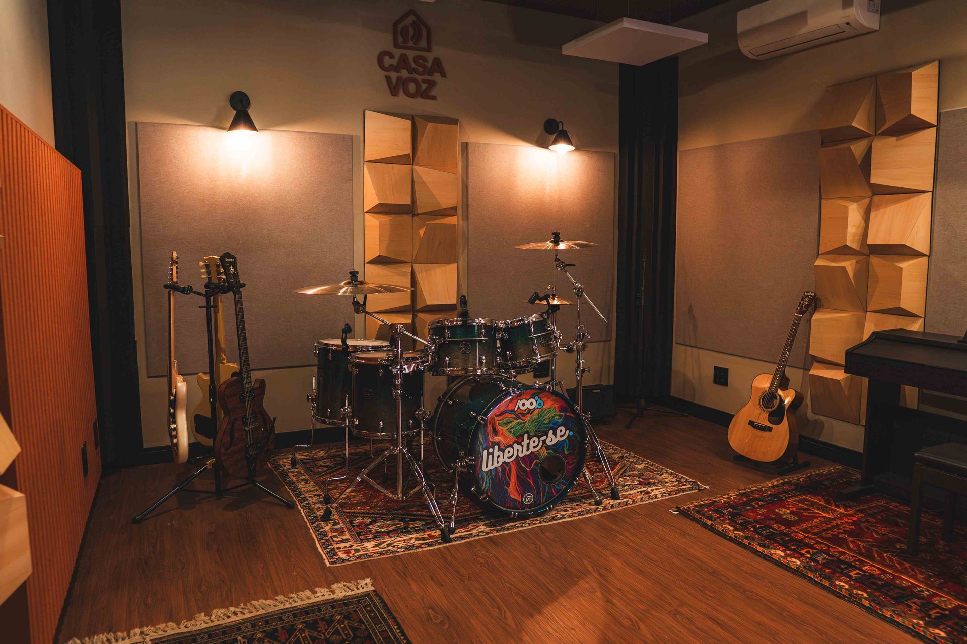 Um estúdio de música com uma bateria no centro, painéis acústicos nas paredes e instrumentos em suportes.