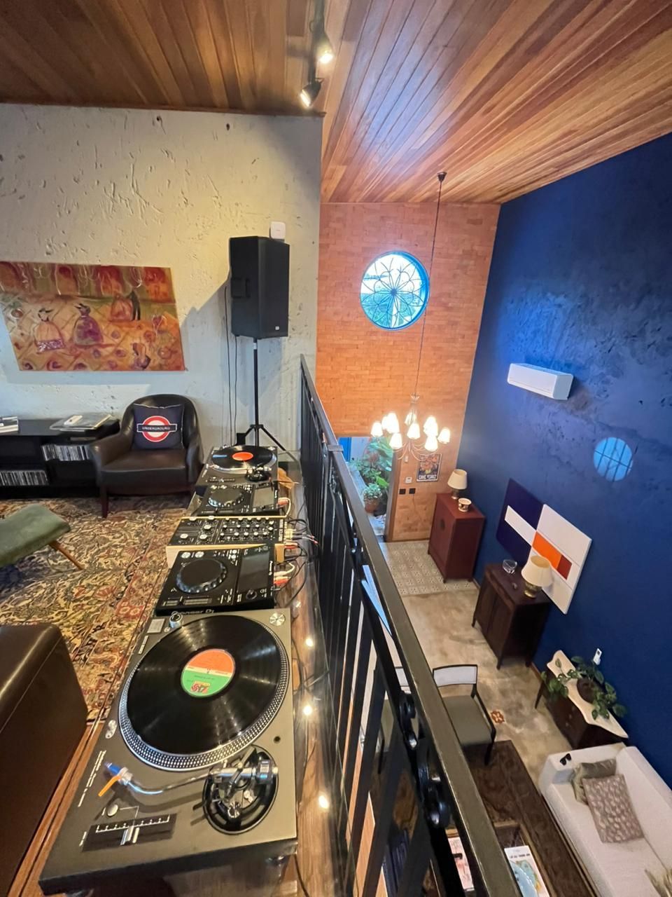 Equipamento de DJ numa varanda com vista para uma sala de paredes azuis, mobilada e com vista para o exterior.