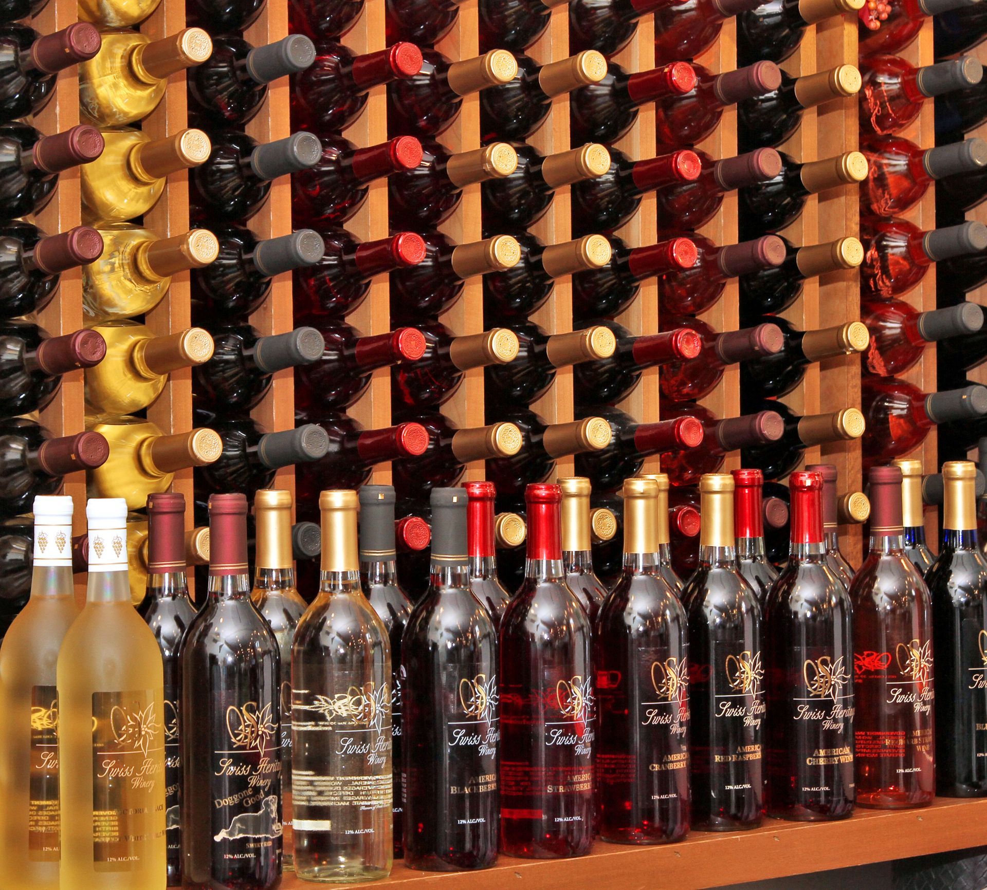 Wine bottles displayed in wooden racks, featuring various red, white, and gold labels and bottles.