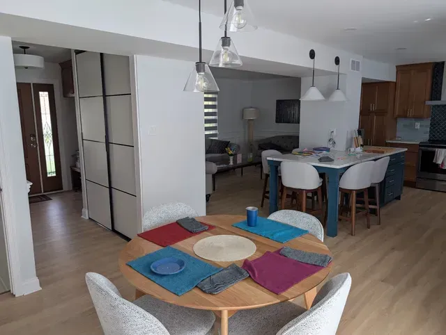 Dining room with round table set for four, leading to a kitchen with island and living room.