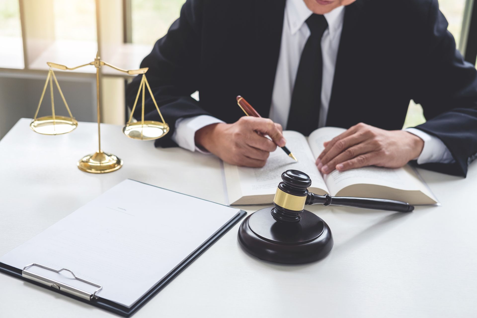 A professional in a suit writes in a book next to a gavel, scales of justice, and a clipboard on a desk — Mitchell Playford & Radburn Solicitors in Grafton, NSW 
