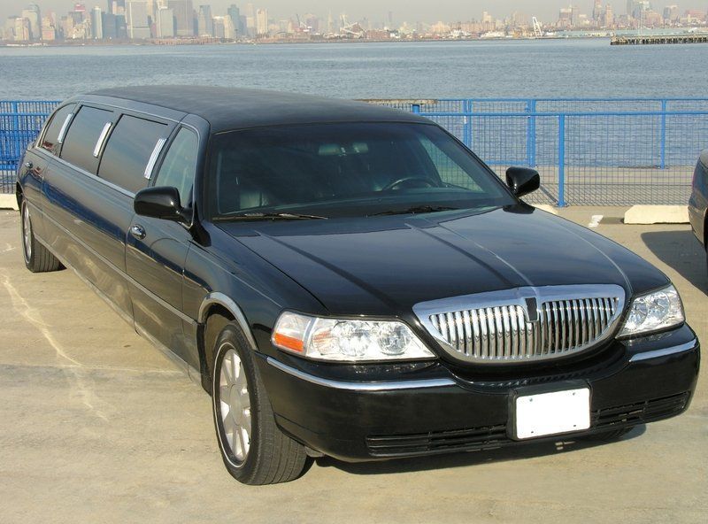 A black lincoln limousine is parked in a parking lot