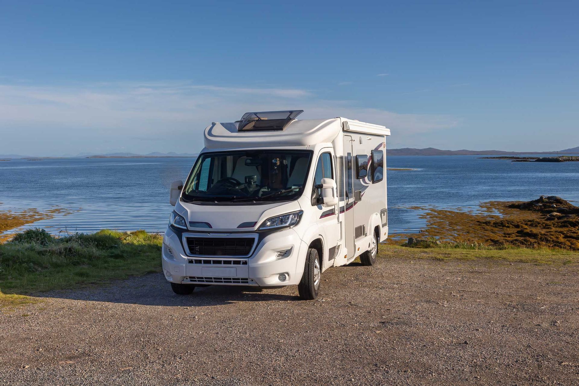A white rv is parked on a gravel road next to the ocean. A white rv is parked on a gravel road next to the ocean.
