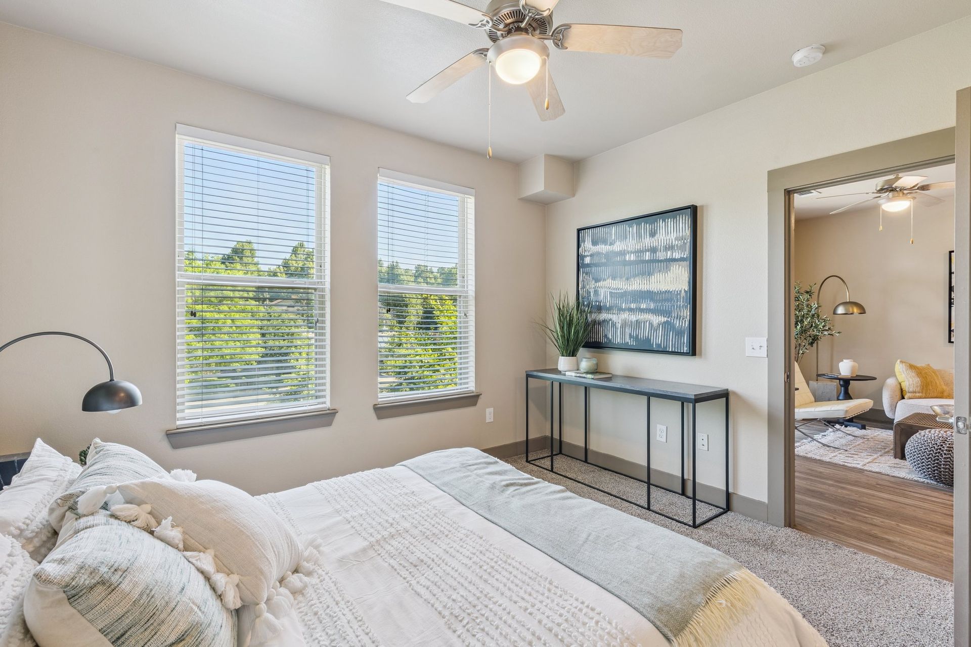 Bedroom with bed, windows, artwork, and a doorway to another room.