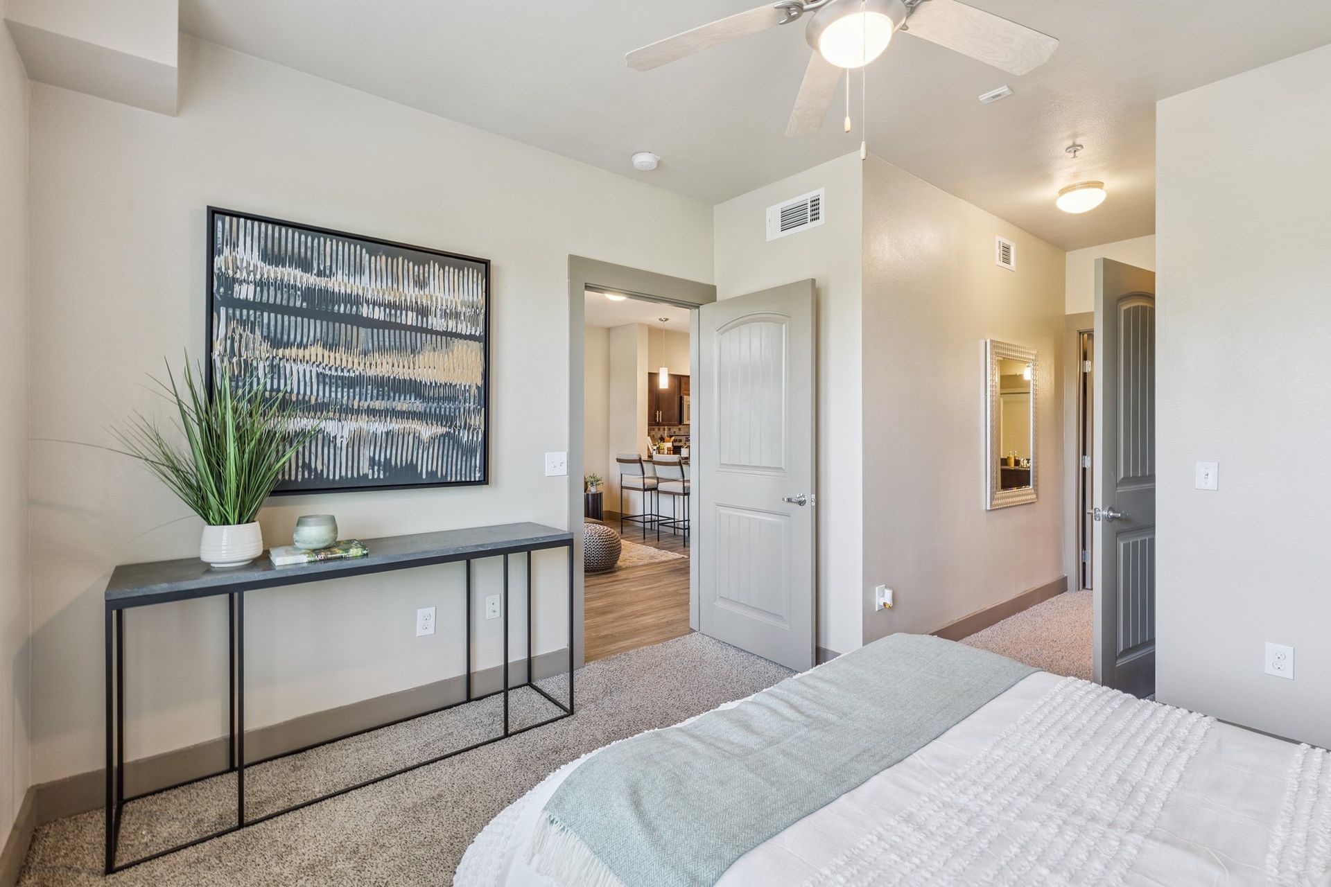 Bedroom with bed, neutral walls, art, a console table with decor, and a doorway.