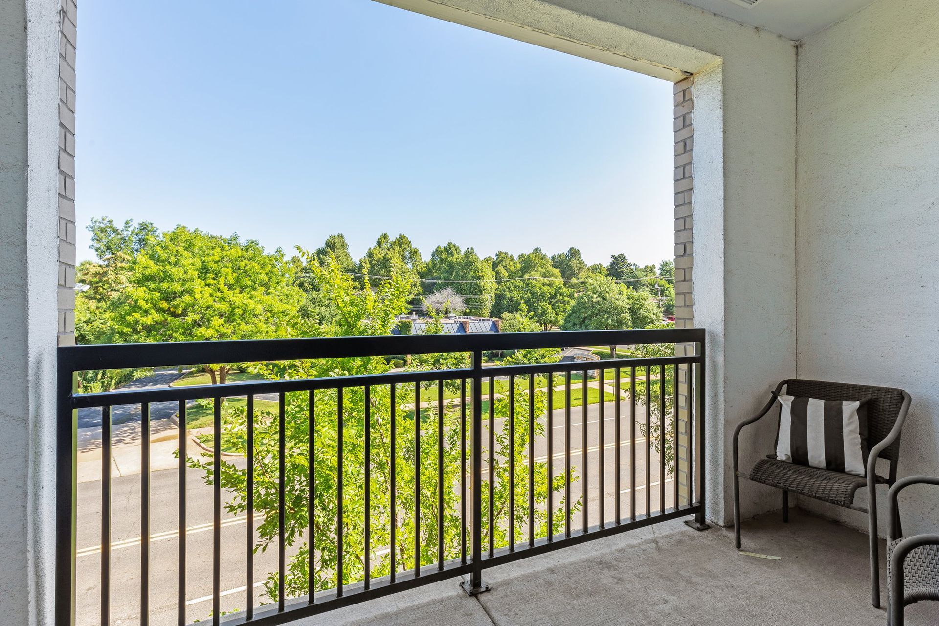 Balcony with black railing and chair overlooking trees and blue sky.