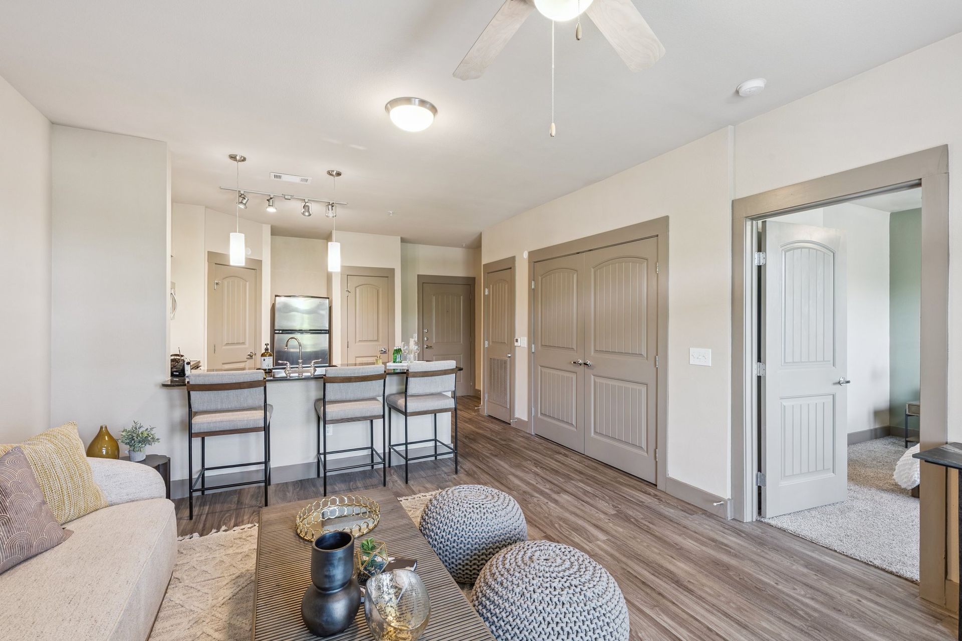 Open-concept living space with a kitchen bar, sofa, wooden floors, and a view into a bedroom.
