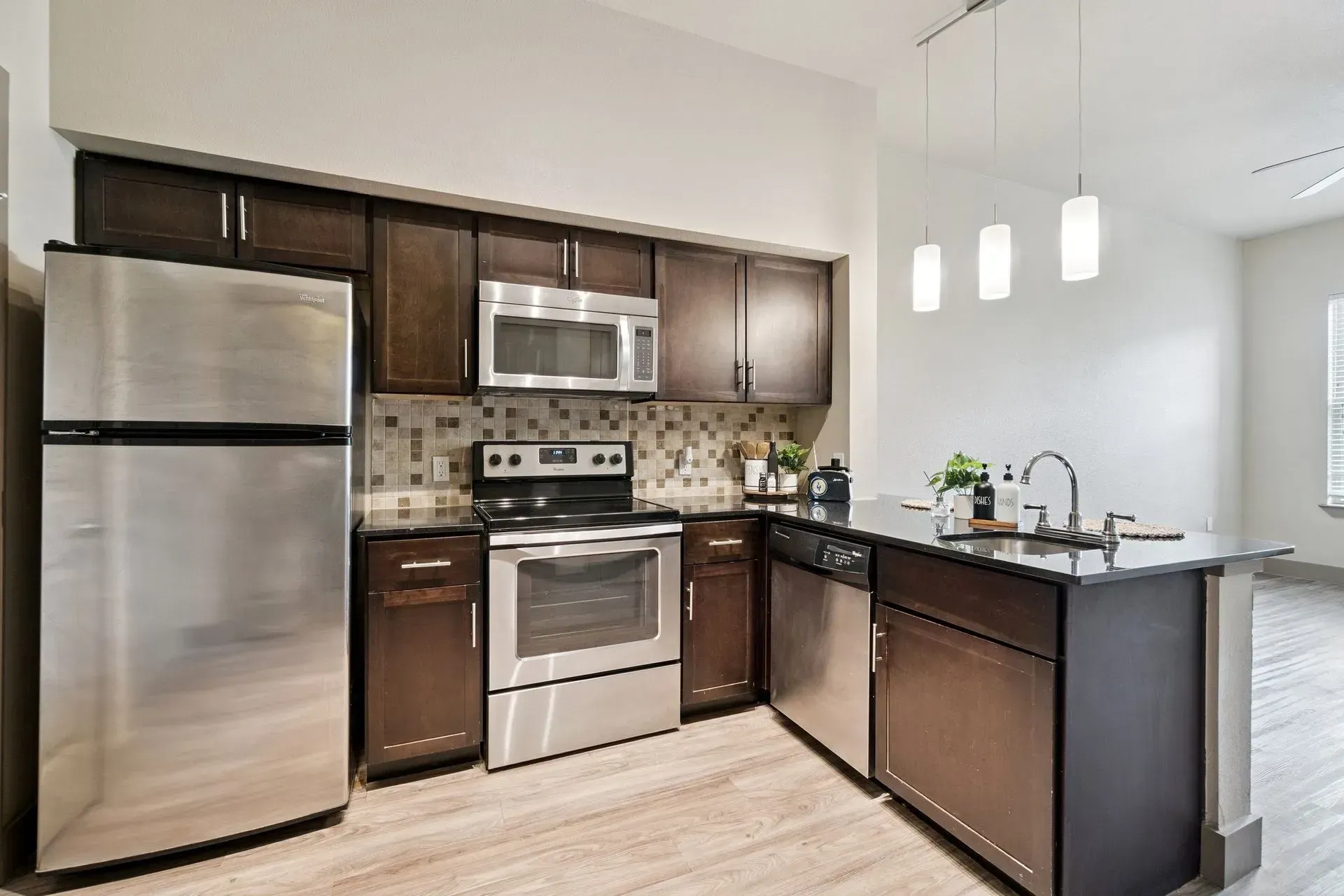 Kitchen with island and bar stools, dark granite counters, stainless steel appliances, and wooden cabinets.