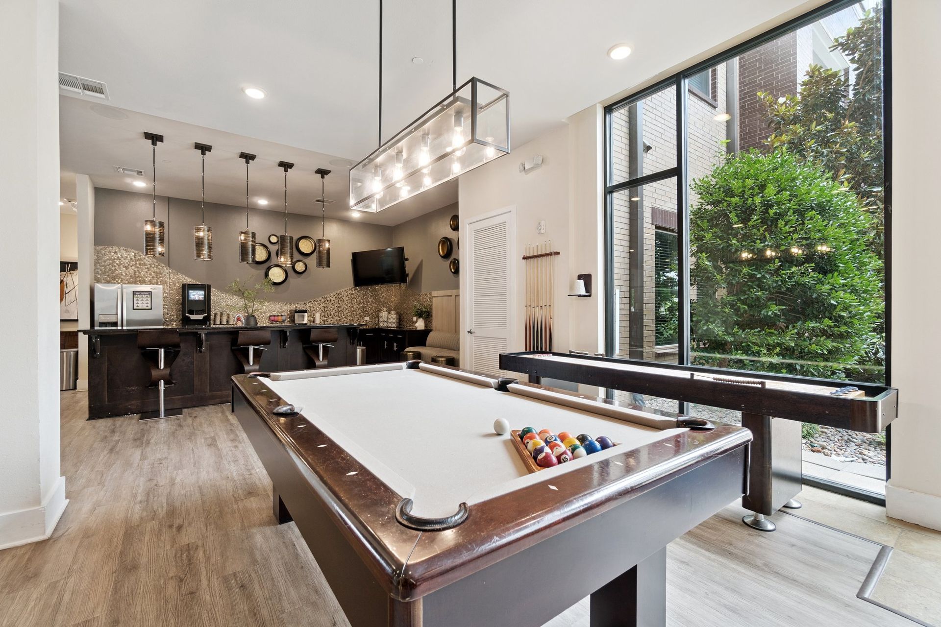 Pool table in a lounge area with a bar and large window overlooking greenery.