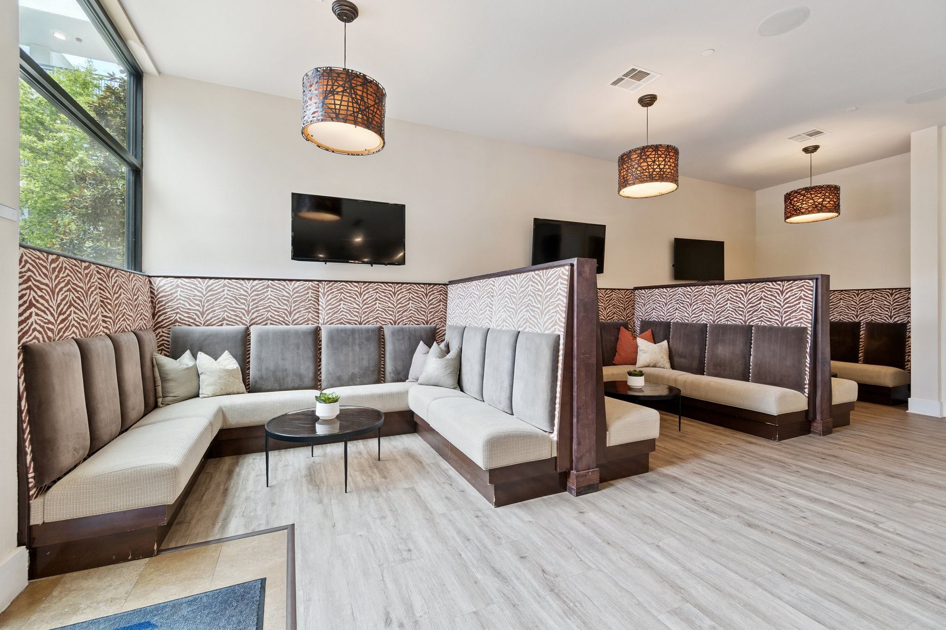Lounge area with booths, beige and brown tones, pendant lights, and two TVs.