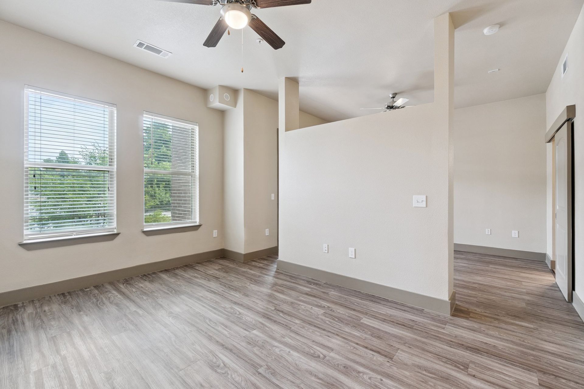 Empty room with hardwood floors, two windows, and a ceiling fan.