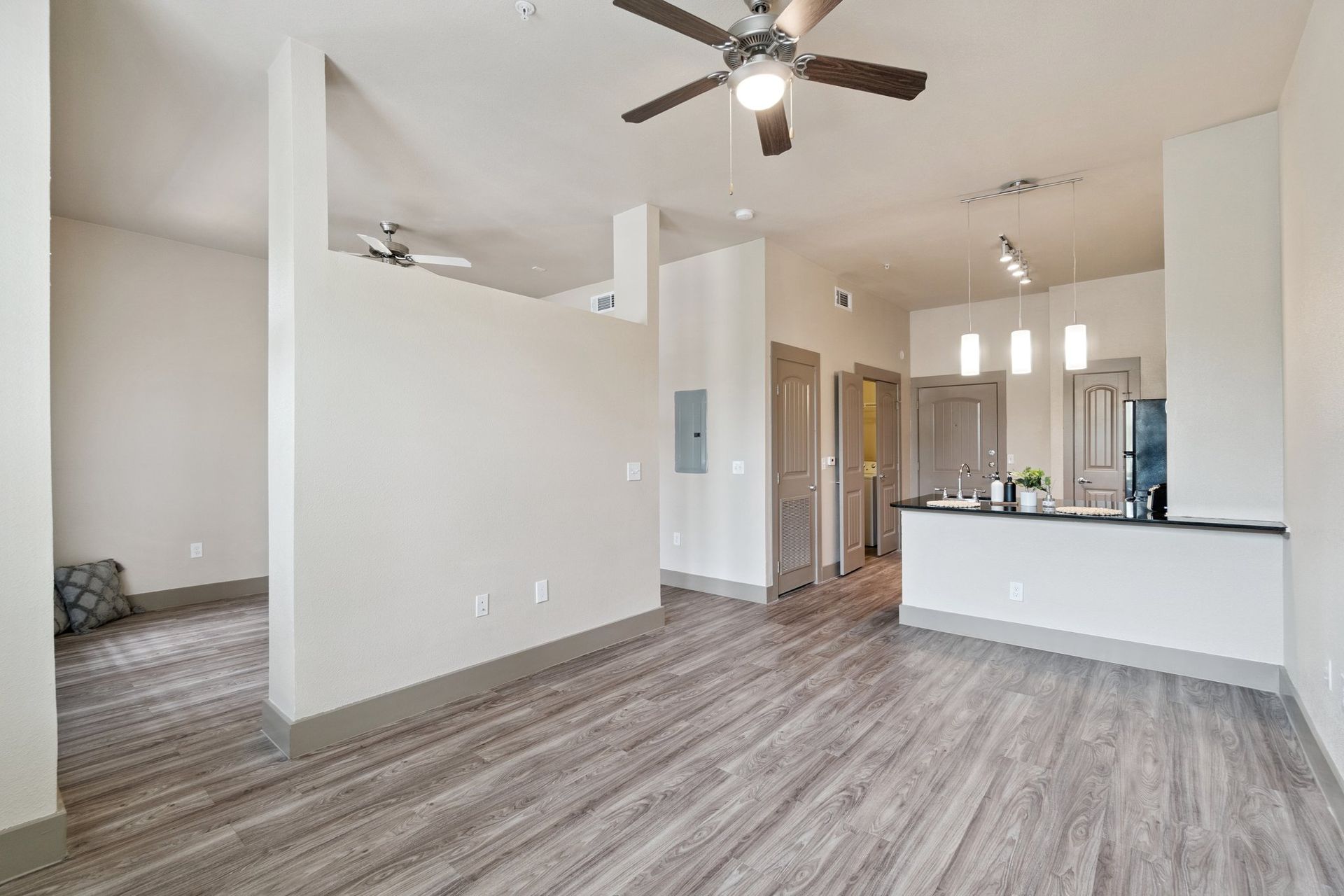 Empty apartment interior with wood-look flooring, neutral walls, and a partial wall separating living areas.