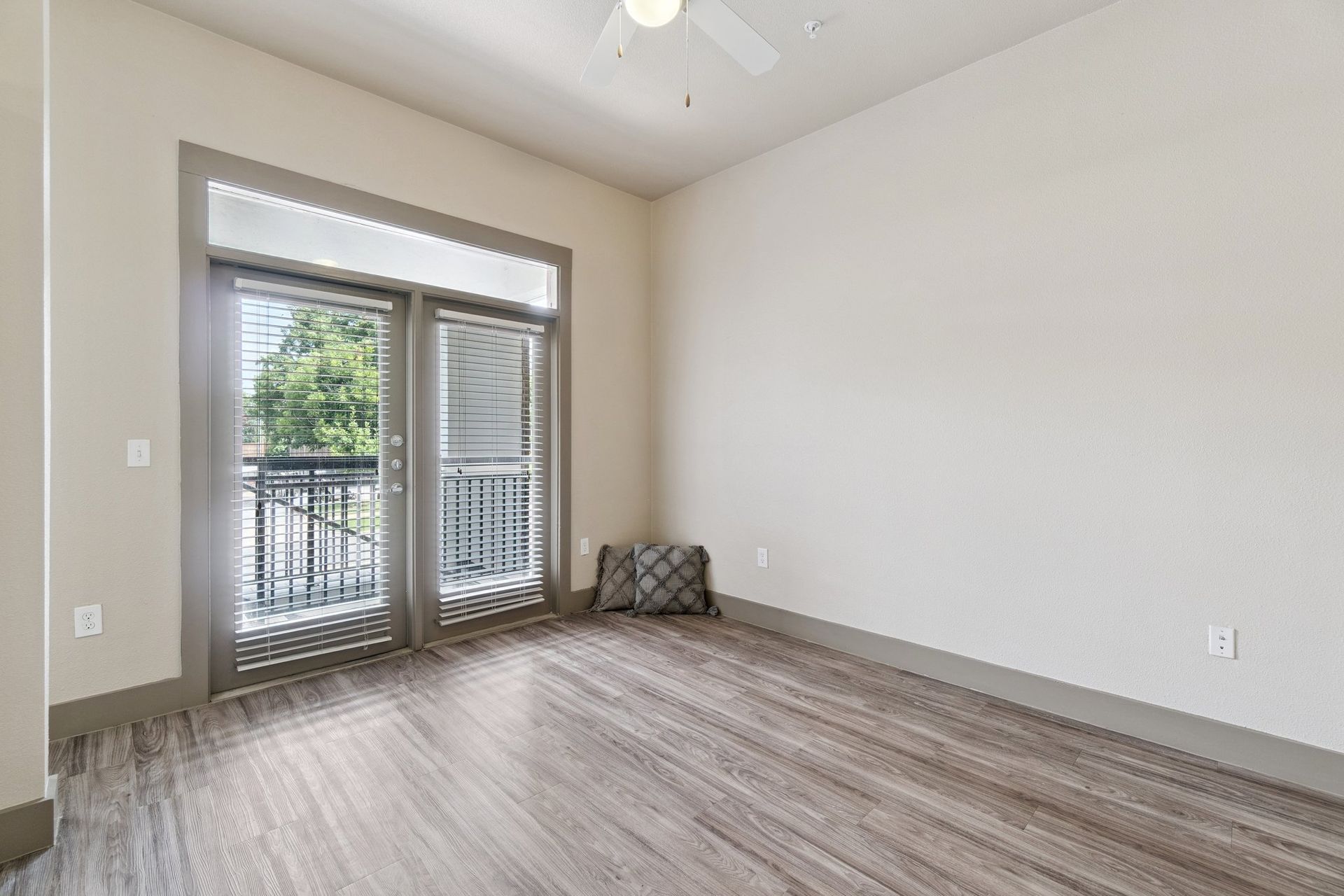 Empty room with wood-look flooring, balcony doors, and a decorative pillow.