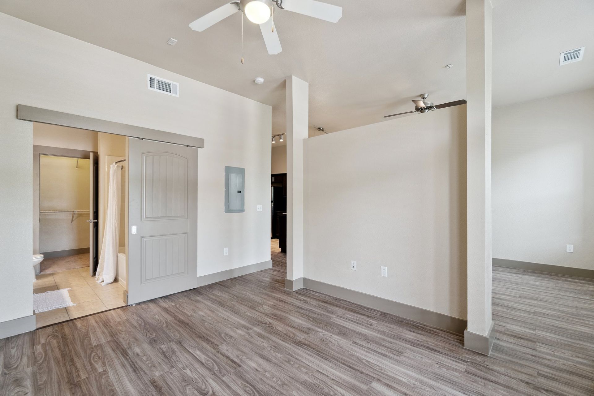 Modern apartment interior with light wood flooring, neutral walls, and sliding door to bathroom.