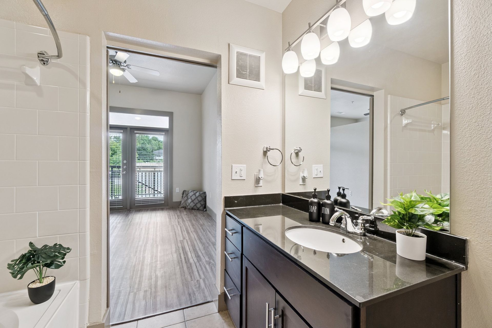 Bathroom with dark vanity, large mirror, and open doorway to a living area with a balcony.