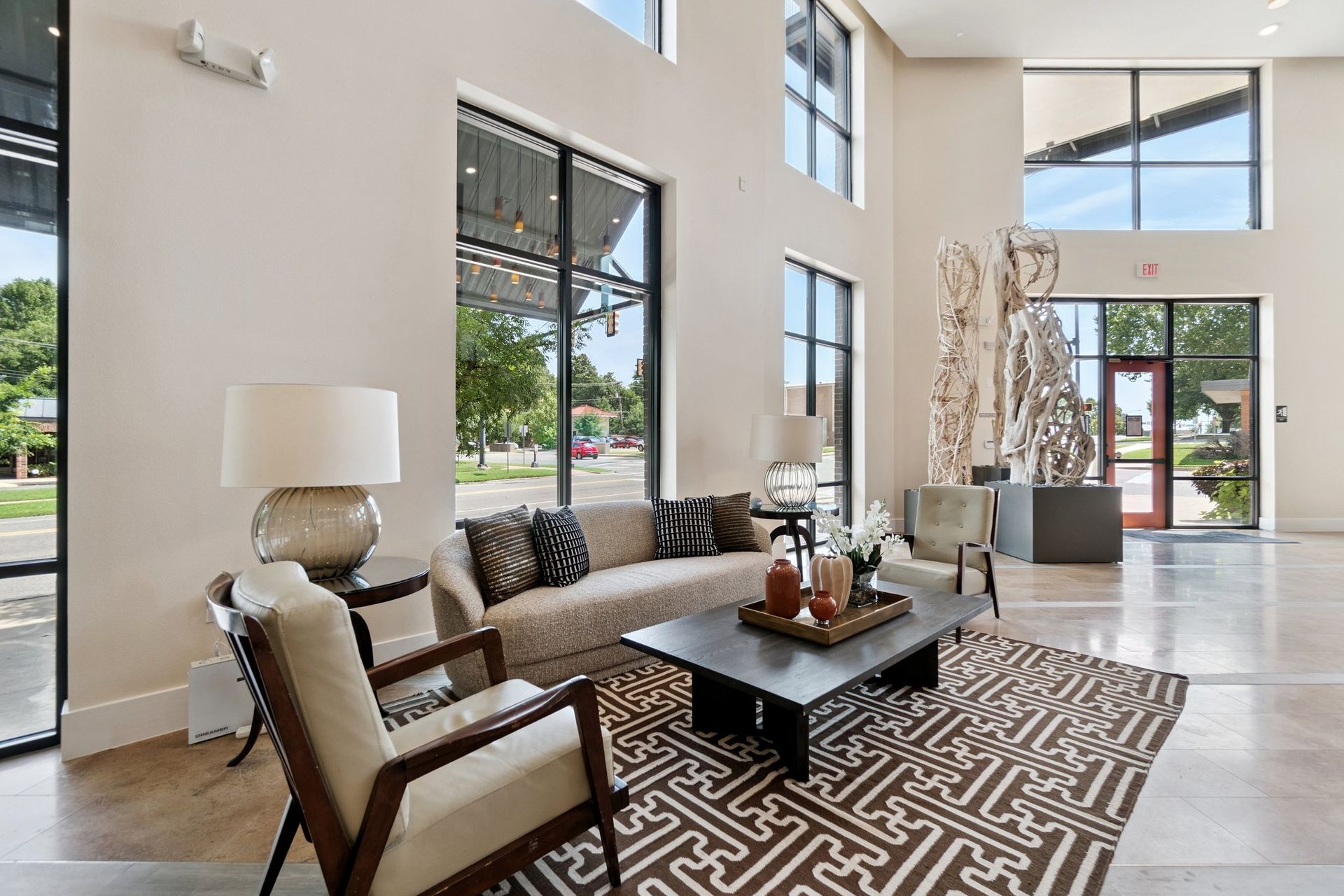 Lobby with seating area: tan sofa, patterned rug, large windows, artwork, and a red door.