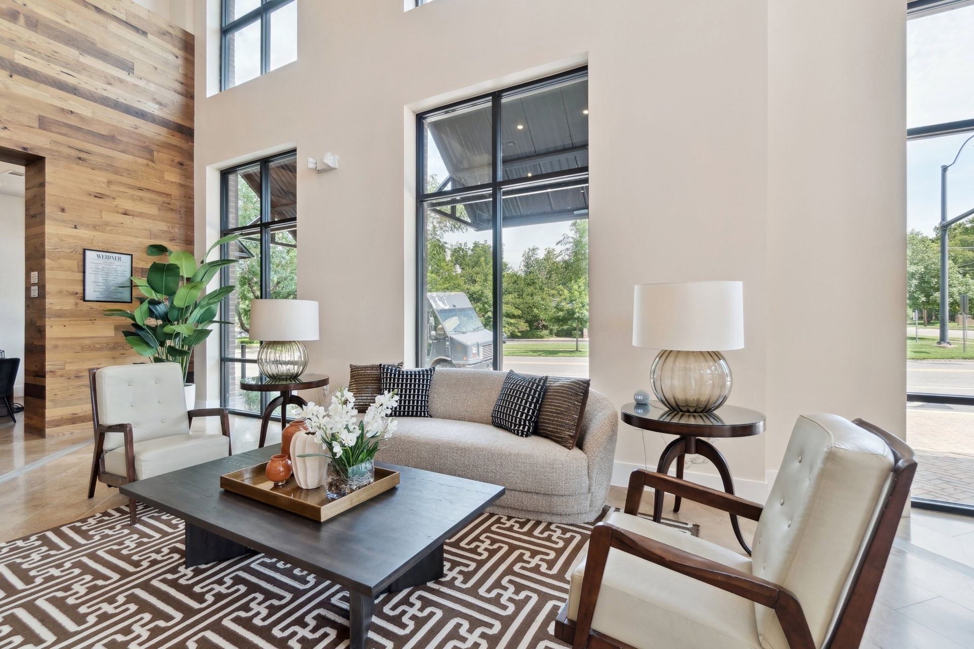 Lobby with tan walls, wood accent wall, sofa, chairs, and large windows with outdoor view.