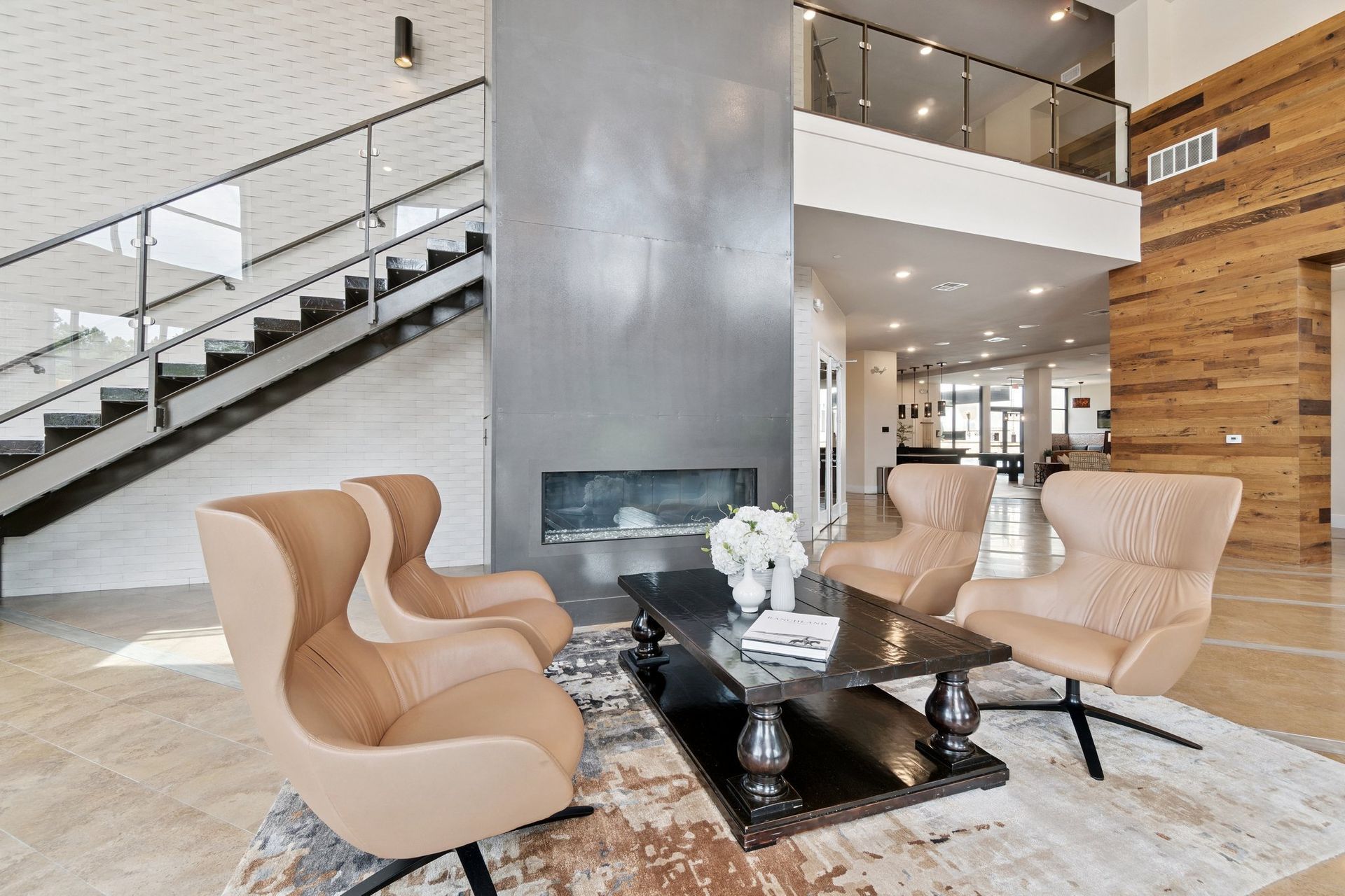 Modern living room with fireplace, chairs, stairs, and wooden accent wall.