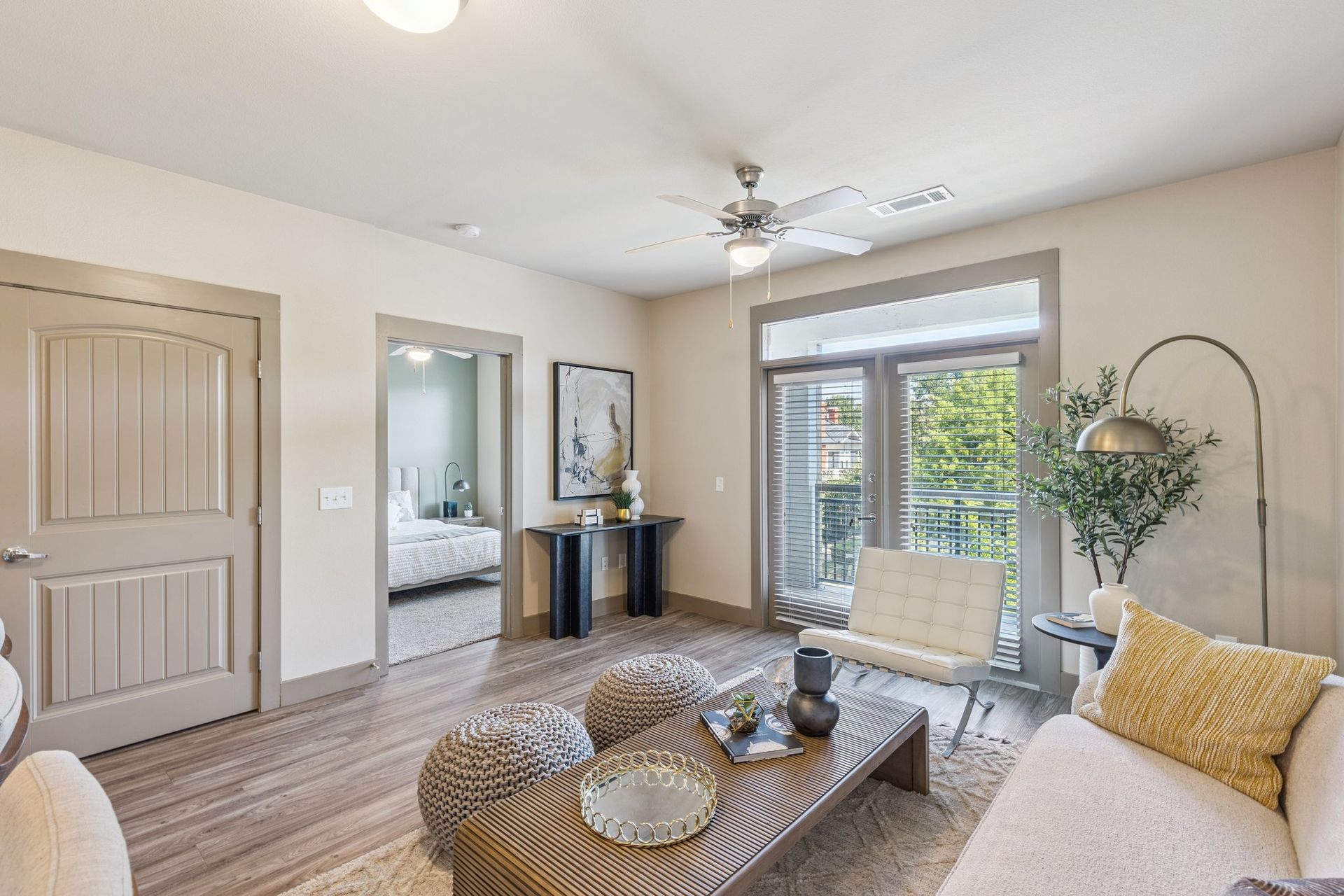 Living room with open doorway to bedroom, balcony access, neutral tones, wood floors, decorative elements.